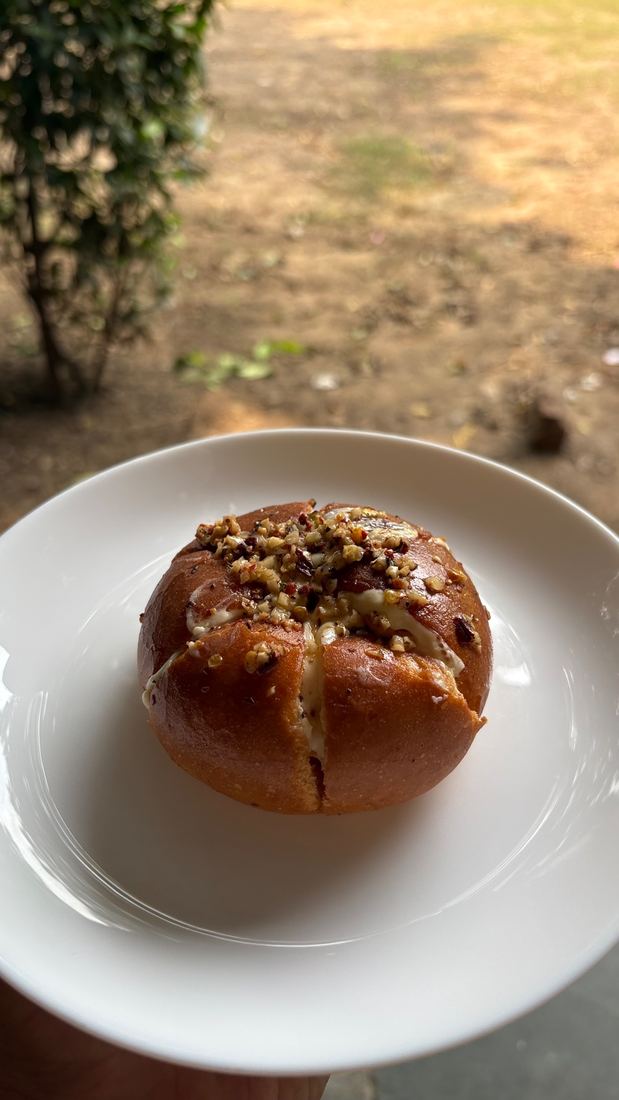 A golden Korean bun split open with cream cheese and a crunchy nut topping, held on a white plate